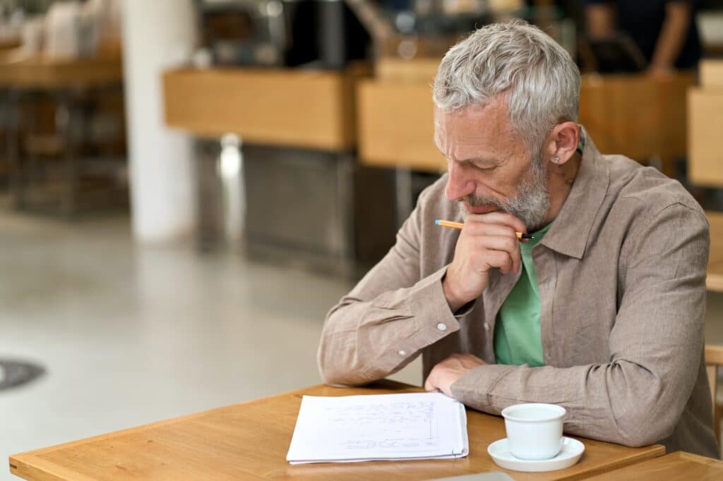 Thoughtful old business man writing in notebook taking notes and thinking.