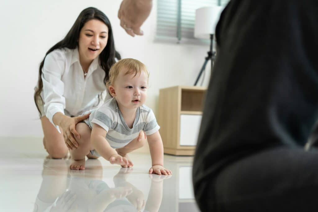 Caucasian baby boy child crawling with parents support in house.