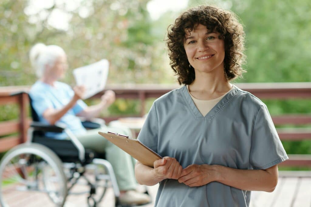 Happy young nurse or caregiver with clipboard looking at camera