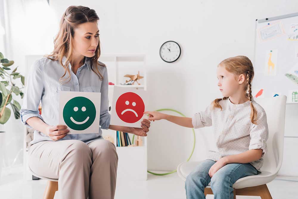 adult psychologist showing happy sad emotion faces cards child