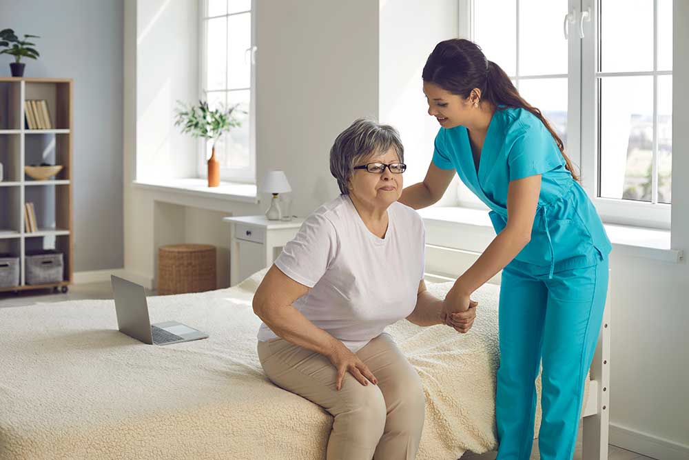 smiling caring nurse supporting patient assisting senior woman get up from bed
