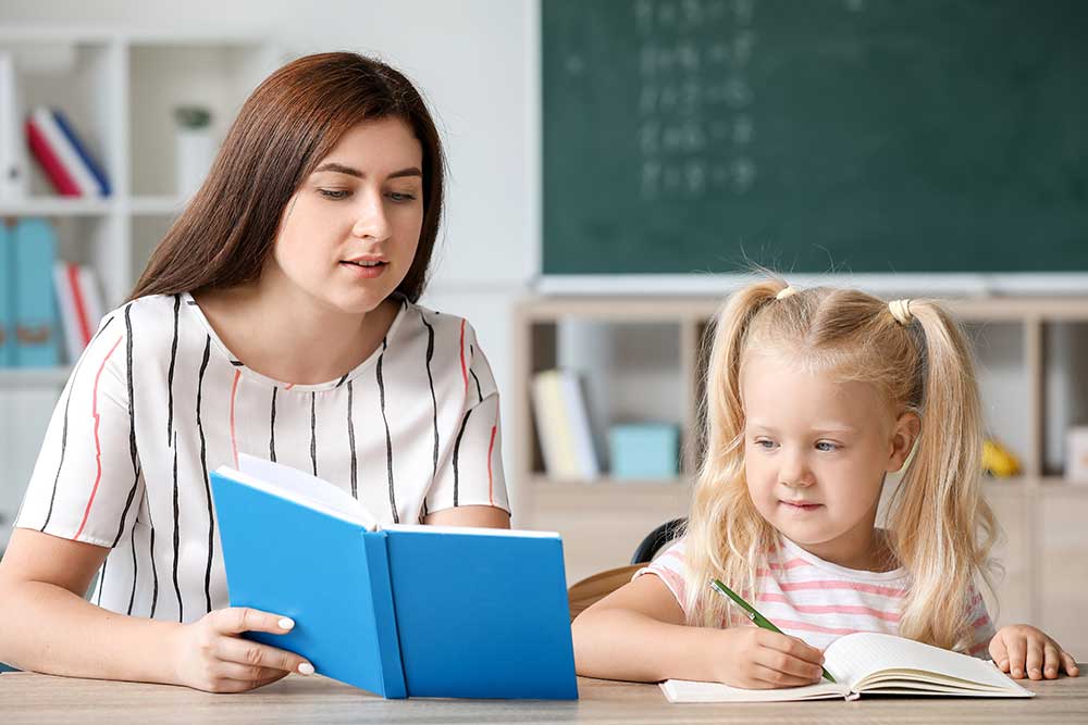 teacher helping little girl to do task in classroom