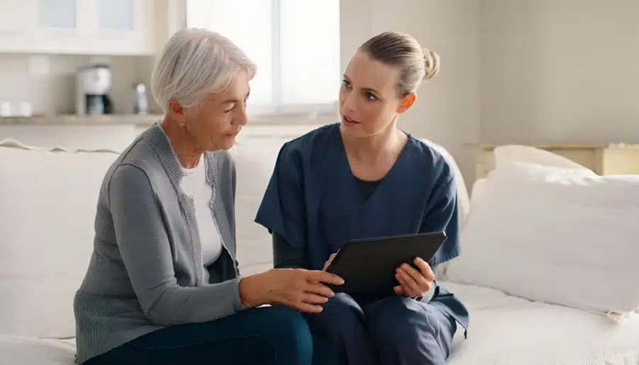 consultation tablet nurse with senior woman sofa living room nursing home