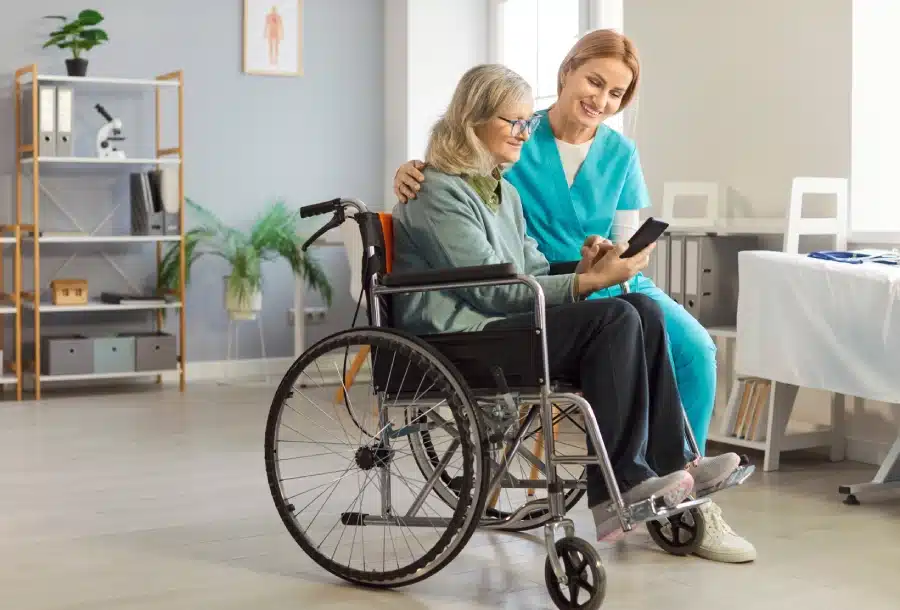 healthcare worker assists woman wheelchair by explaining medical app her smartphone