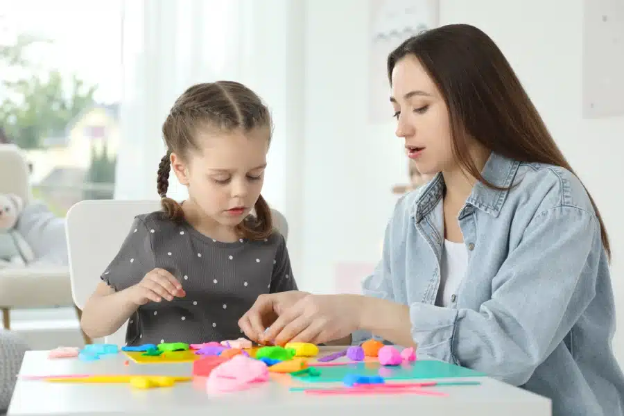 mother her daughter sculpting with play dough table indoors